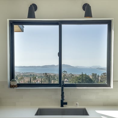 A kitchen with a view of a mountainous coastline thanks to the Andersen® 100 Series Gliding Window above the sink.